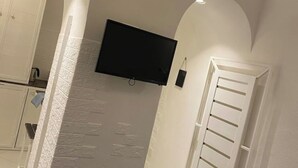 Een kamer met een witte baksteenmuur, een wandgemonteerde flatscreen-tv, een witte deur met een handdoek eraan en een witte garderobe.
