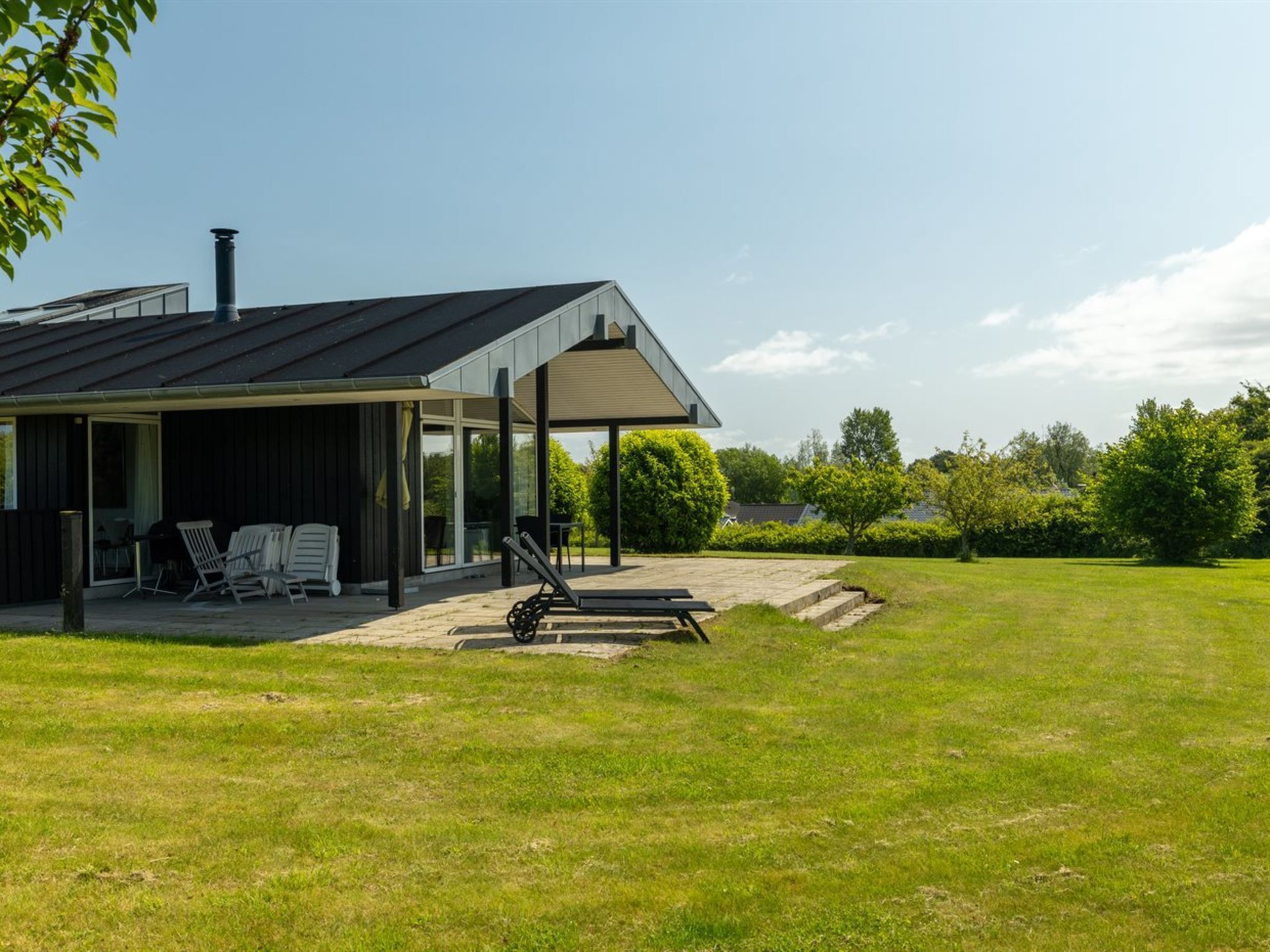 Une maison moderne dotée d’un patio couvert, d’un espace salon extérieur et d’une pelouse verdoyante.