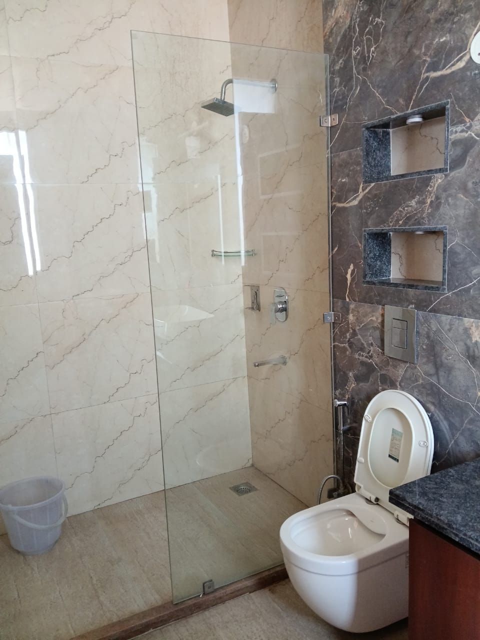 Ein modernes Badezimmer mit einer gläsernen Duschkabine, einer Toilette und Marmorwänden.