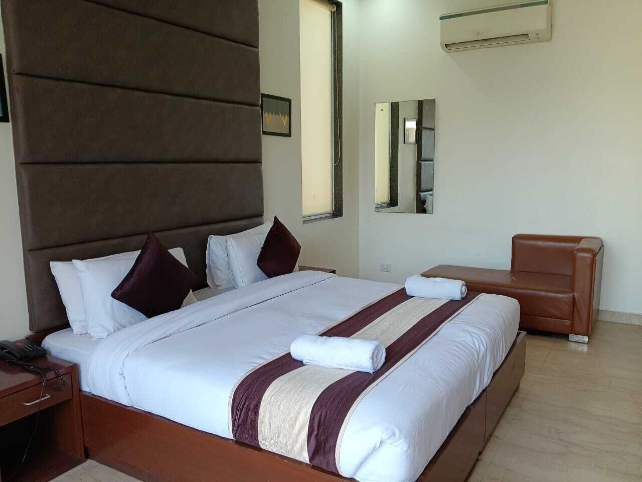 A hotel room with a large bed, a wooden nightstand, a brown leather chair, and a wall-mounted air conditioner.