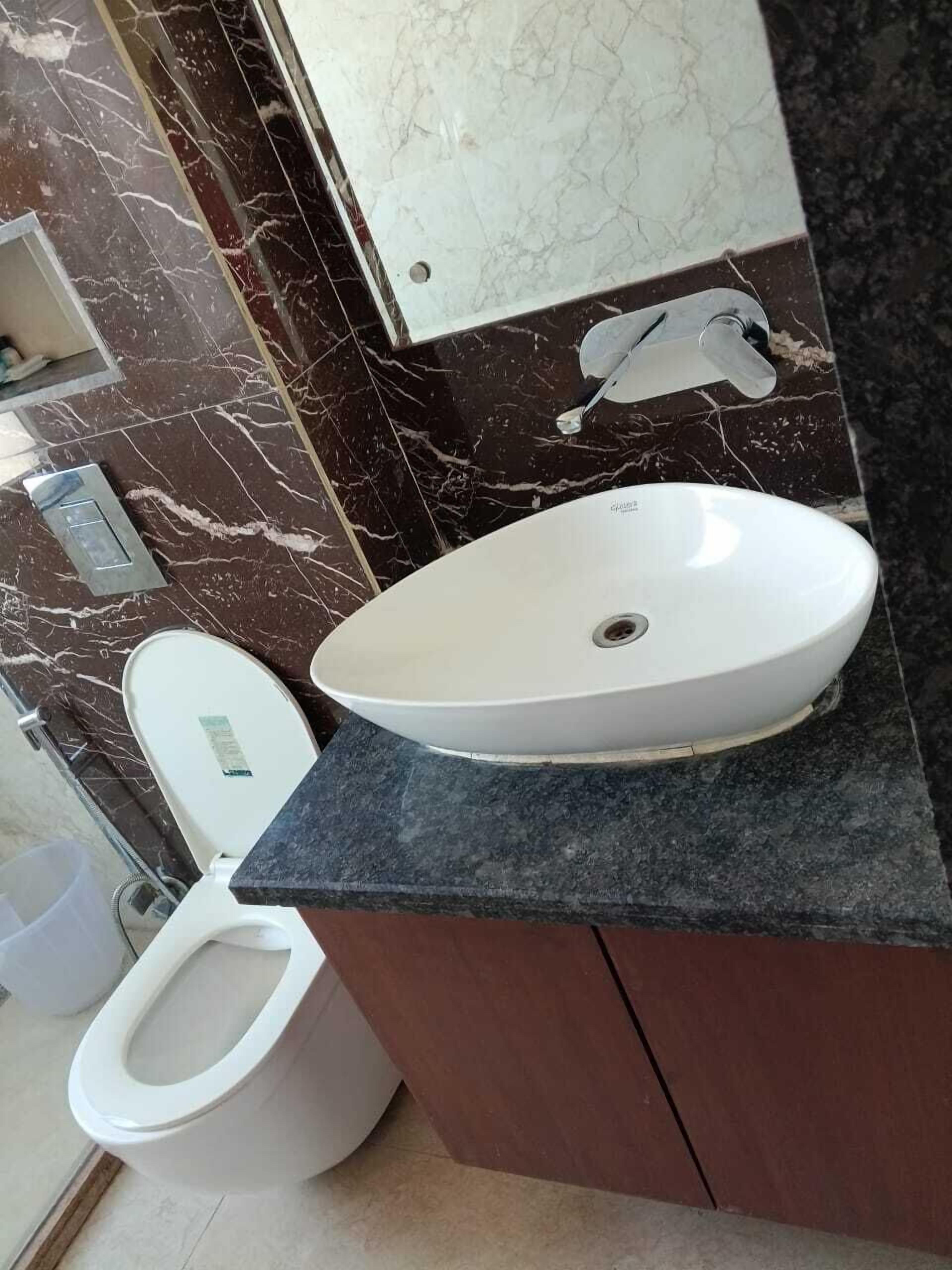 A bathroom with a white toilet, a white sink on a dark countertop, and a marble backsplash.