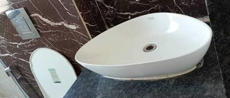 A bathroom with a white toilet, a white sink on a dark countertop, and a marble backsplash.