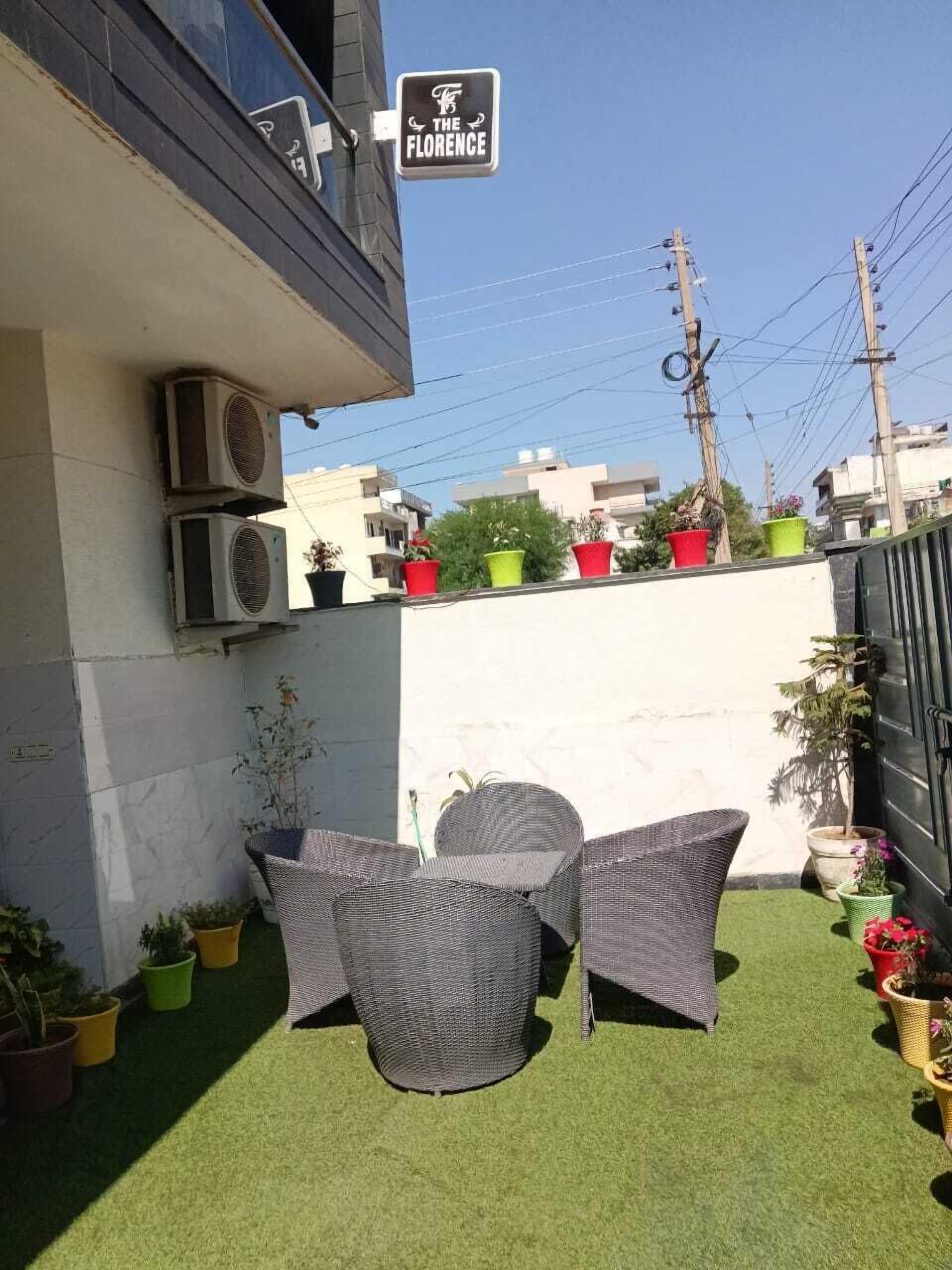 An outdoor seating area with two wicker chairs and a small table, surrounded by potted plants and a sign for "The Florence".