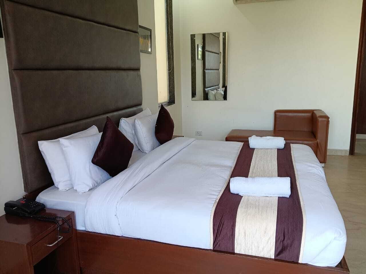 A hotel room with a large bed, a bedside table with a phone, a mirror, and a brown leather chair.