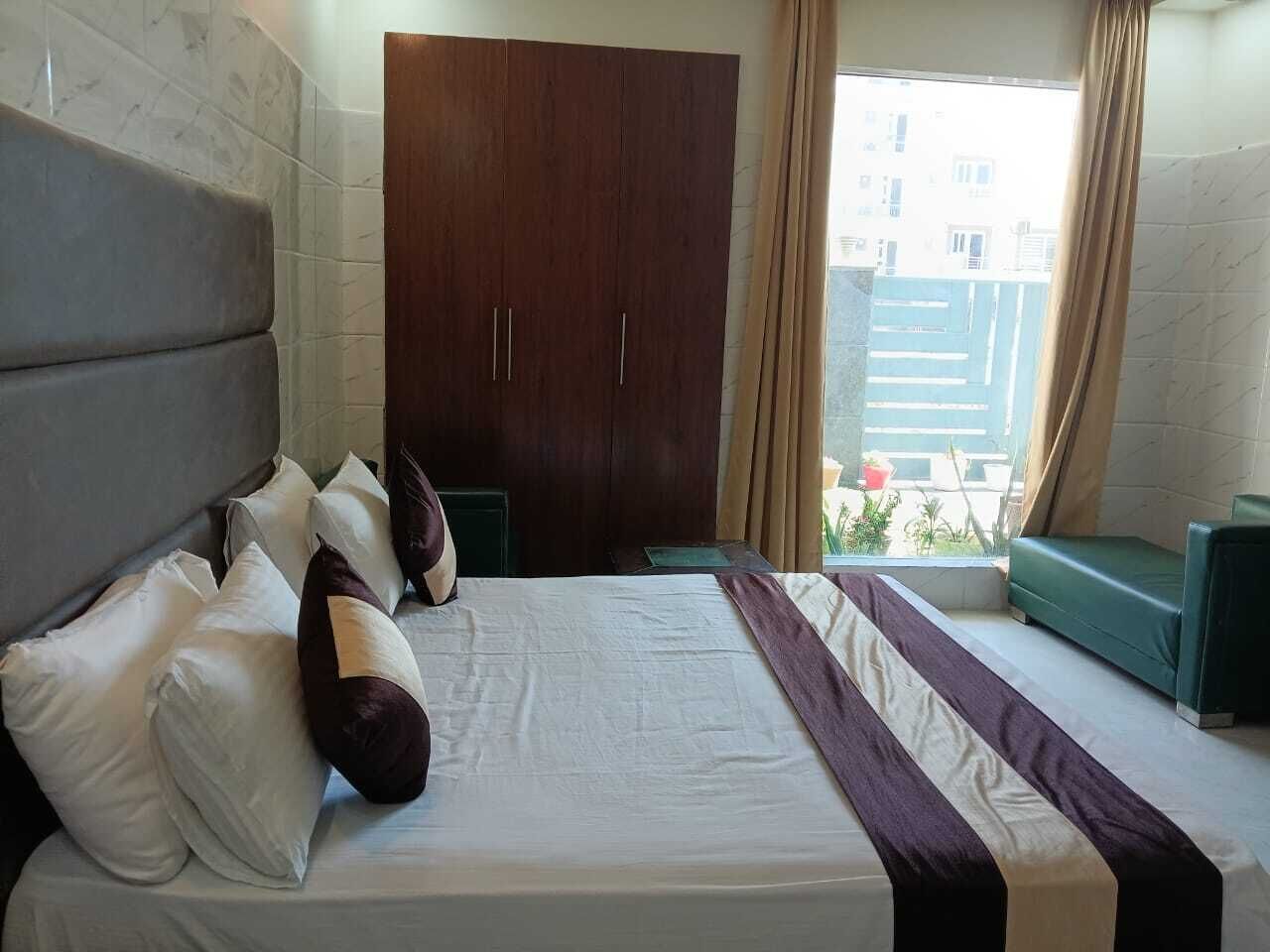Ein Hotelzimmer mit einem großen Bett, einem Schrank, einem Fenster mit Vorhängen und Blick auf Gebäude.