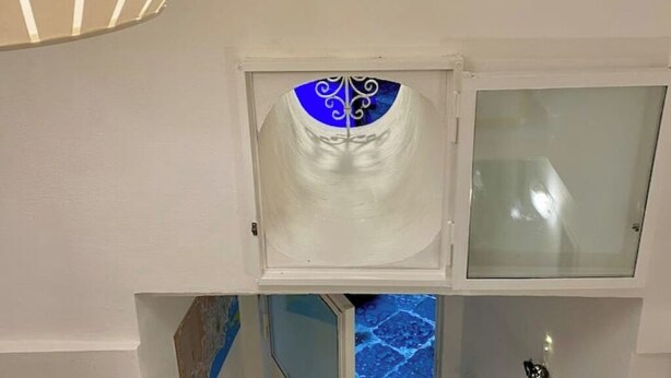 Una habitación con un armario blanco y una ventana pequeña con un diseño azul y blanco decorativo.