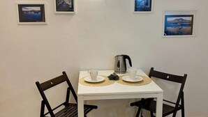 Un pequeño comedor con una mesa blanca y dos sillas, una tetera y dos tazas sobre individuales.