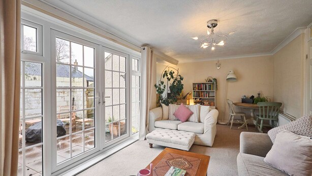A spacious living room with a large sliding glass door leading to an outdoor area, a comfortable sofa, a coffee table with a magazine, and a bookshelf. - Host Stay Trinity Way (Keswick)