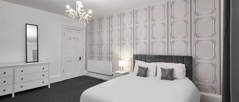 A bedroom with a large bed, a dresser, a nightstand, a lamp, and a chandelier.