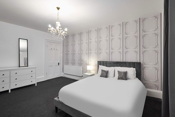 A bedroom with a large bed, a dresser, a nightstand, a lamp, and a chandelier.