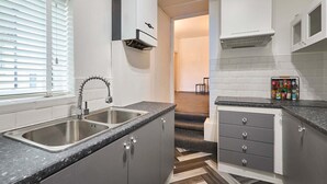 A modern kitchen with a double sink, grey cabinets, a herringbone-patterned floor, and a window with blinds. - Host Stay Queen Street Apartment (Morpeth)