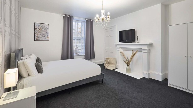 A bedroom with a large bed, a TV, a fireplace, and a window with curtains. - Host Stay Queen Street Apartment (Morpeth)