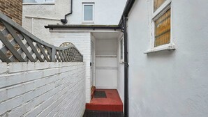 A narrow alleyway with a red step leading to a door, white walls, and a metal gate. - Host Stay Queen Street Apartment (Morpeth)