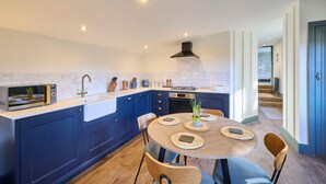A modern kitchen with a central island, built-in appliances, and a dining area with a round table and chairs. - Host Stay The Lodge (Whitby)