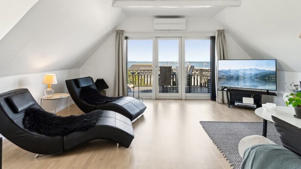 A modern, well-lit room with a curved black sofa, a small table with a plant, and a TV on a stand. - "Mari" - 150m from the sea by Interhome (Tranekær)