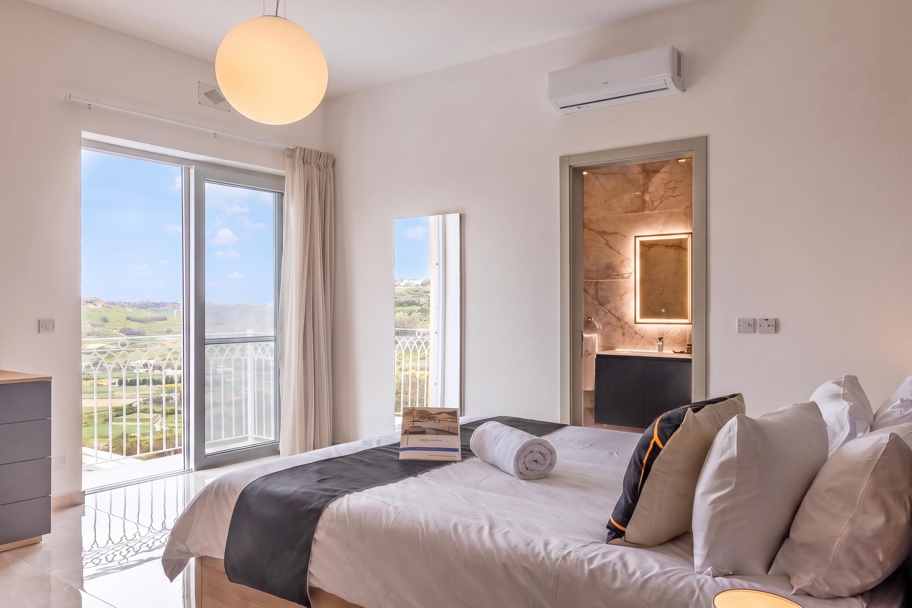 A bedroom with a large bed, a bedside table, a mirror, and a view of the outdoors.