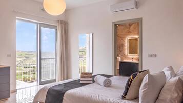 A bedroom with a large bed, a bedside table, a mirror, and a view of the outdoors.