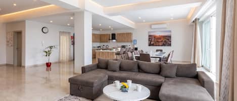 A spacious living area with a sectional sofa, a dining table, and a kitchen in the background.