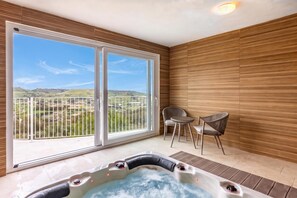 Ein Zimmer mit einer großen Glasschiebetür, die auf einen Balkon führt, sowie einem Whirlpool und zwei Stühlen.