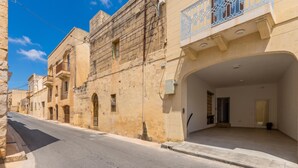A street view of a building with a large arched entrance, multiple windows, and a balcony with metal railings. - Magnifica Gozitan Villa Pool And Jacuzzi (Xaghra)