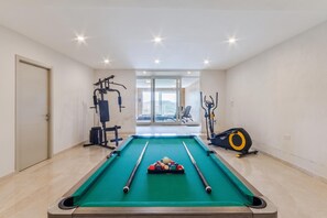 A pool table with balls and cues, a weight machine, and a stationary bike in a room with a door and a view through a glass door. - Magnifica Gozitan Villa Pool And Jacuzzi (Xaghra)