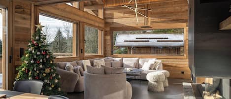 A modern interior with a wooden ceiling, a large window, a fireplace, and a Christmas tree.