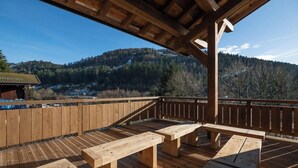 Une terrasse en bois avec des tables de pique-nique, offrant une vue sur un paysage montagneux.