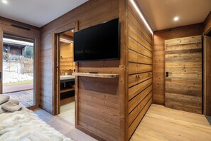 Una stanza moderna con arredamento in legno, una TV a schermo piatto fissata al muro e una porta scorrevole che dà su una zona esterna.