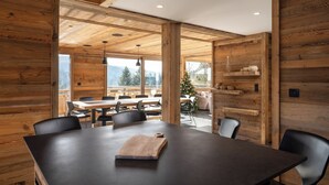 Un intérieur moderne avec une grande table à manger en bois, des chaises noires et une vue sur l’extérieur.
