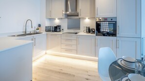 A modern kitchen with white cabinets, a stainless steel sink, a coffee maker, and a built-in oven. - Cosy 2-Bedroom Next to Harlow Town Station (Harlow)