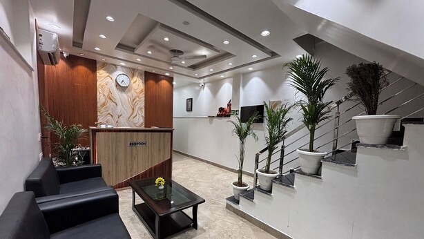 A modern reception area with a reception desk, black sofas, a coffee table, and potted plants.