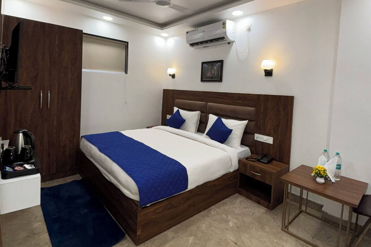 A modern bedroom with a large bed, a wooden wardrobe, a small table with toiletries, and an air conditioning unit.