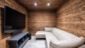 A room with a wooden interior, a flat-screen TV mounted on the wall, a white leather sofa, and a small entertainment unit.
