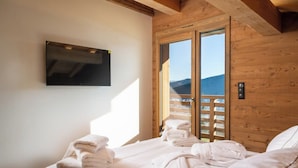 A bedroom with a bed, a TV mounted on the wall, and a view through a sliding door.