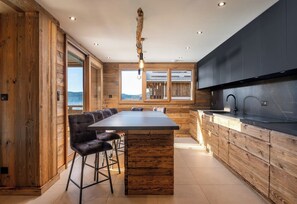 A modern kitchen with a large island, bar stools, wooden cabinetry, and a view of the outdoors.