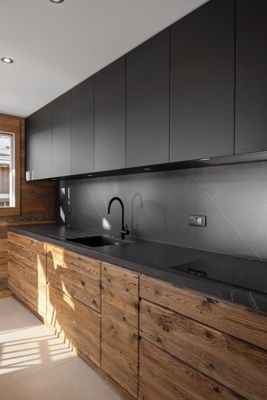 A modern kitchen with dark cabinetry, a black countertop, and a wooden accent wall.