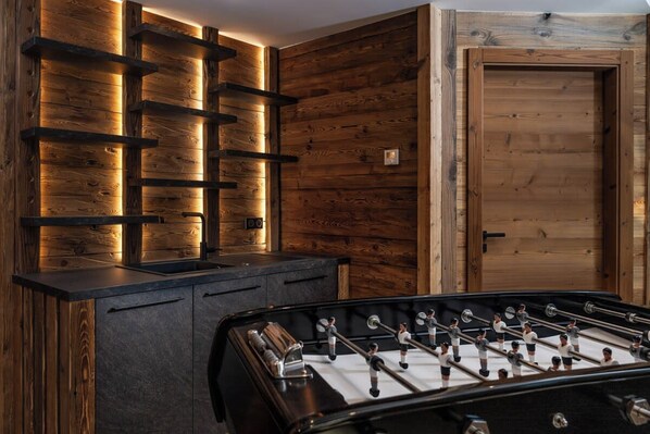 Una habitación con paneles de madera, una mesa de futbolín negra y una puerta con marco de madera.