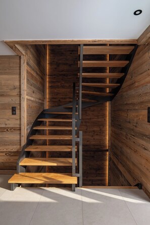 A spiral staircase with wooden steps and metal railings, built into a wall with wooden paneling.