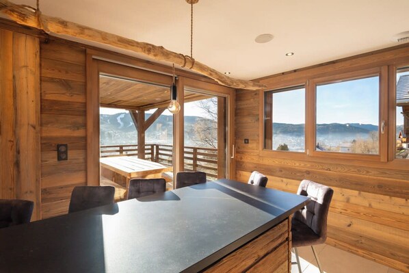 A wooden interior with a large dining table, chairs, and a view of the outdoors.