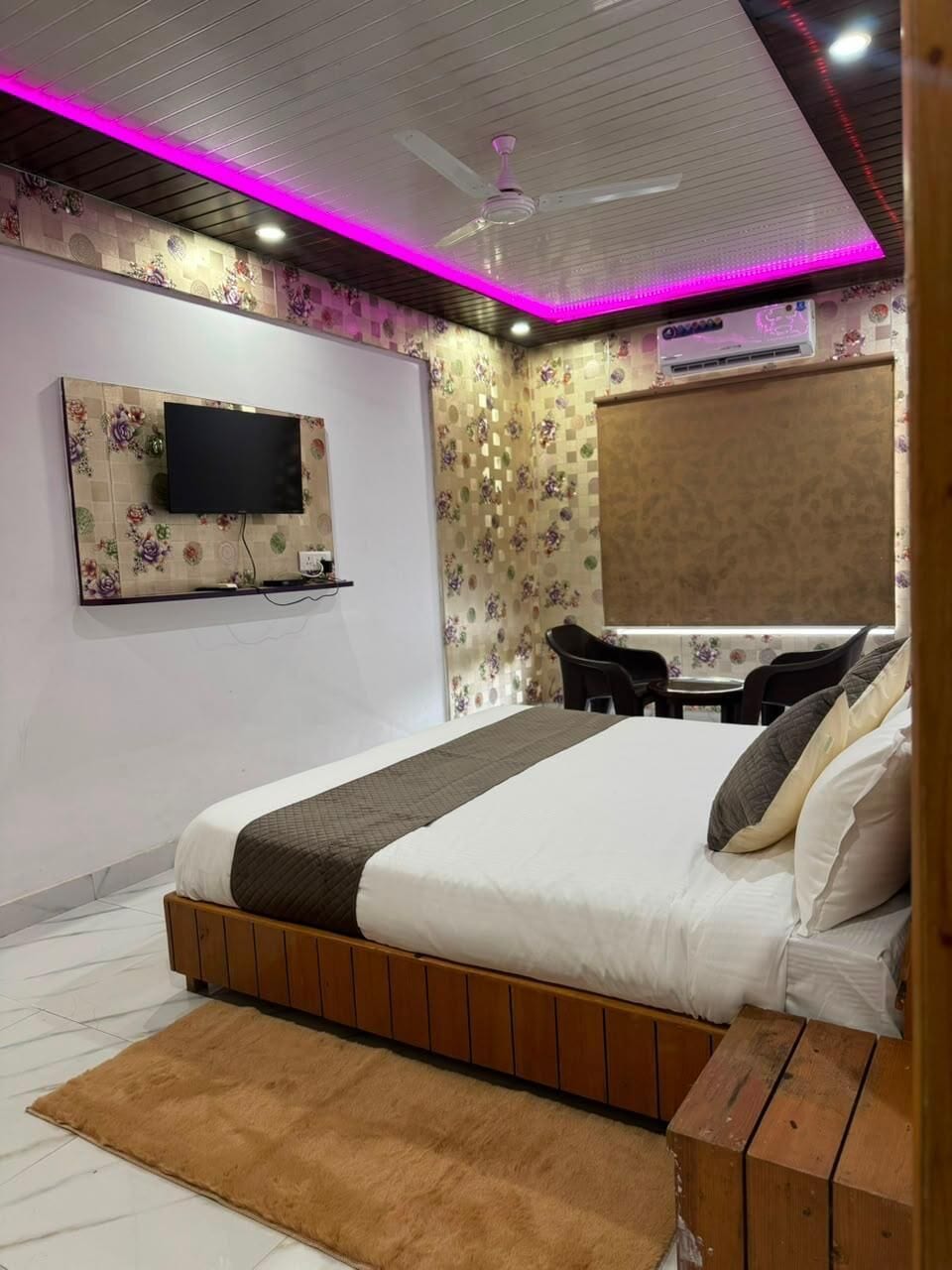 A bedroom with a bed, a TV mounted on the wall, a ceiling fan, and a window with curtains.
