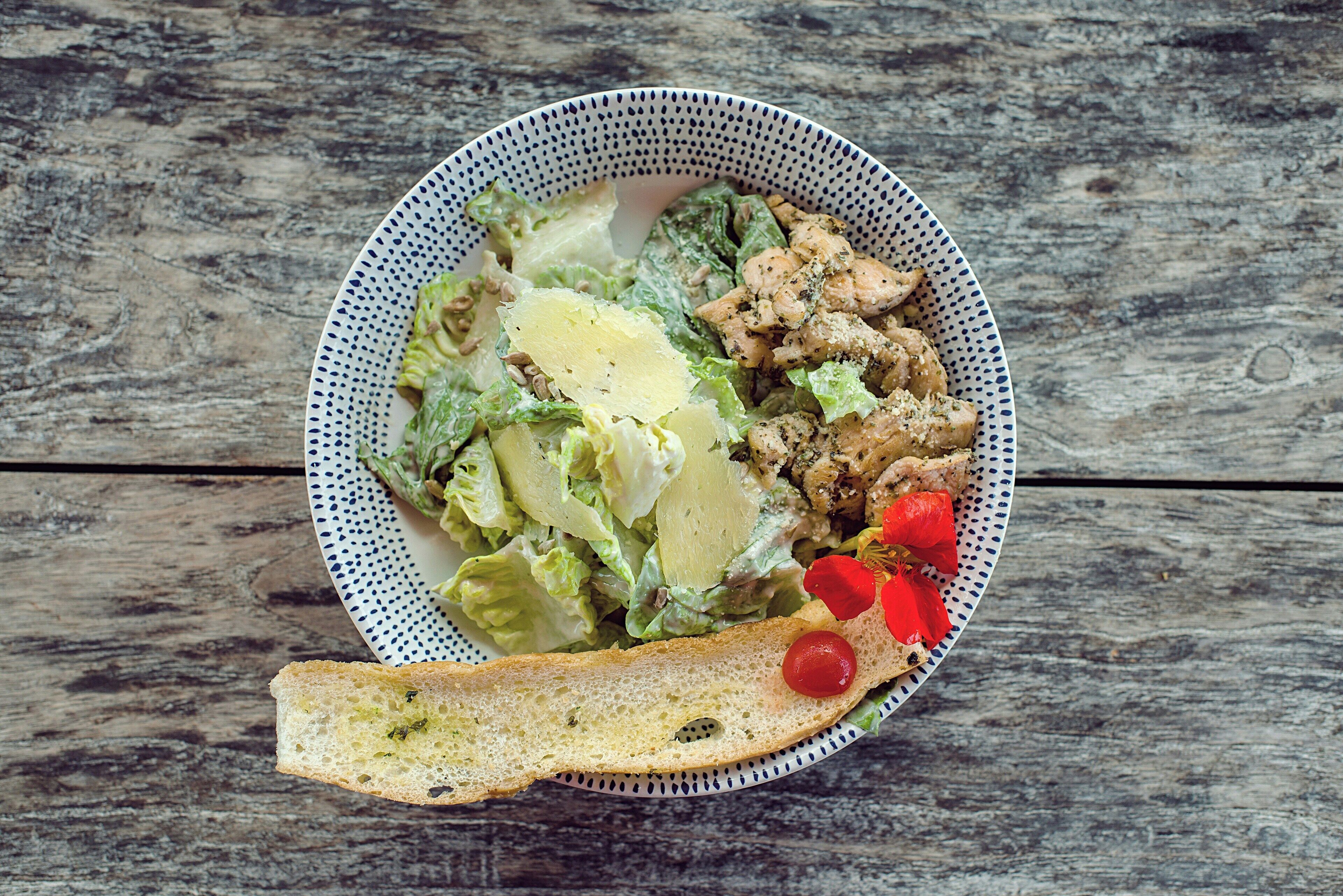 A bowl of salad with lettuce, croutons, and a slice of bread on a wooden table.