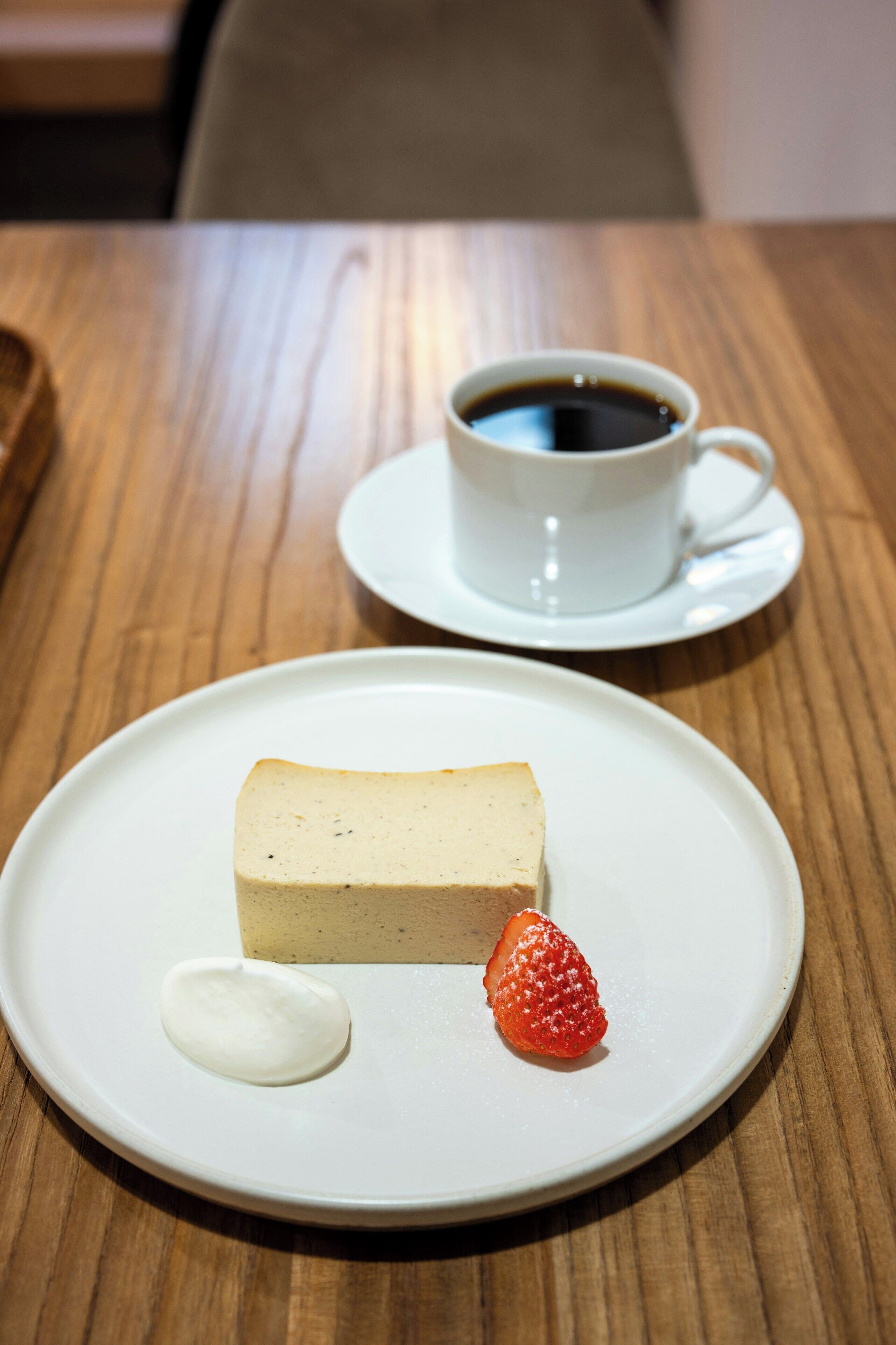 A dessert plate with a cheesecake, a strawberry, and a dollop of cream on a wooden table.