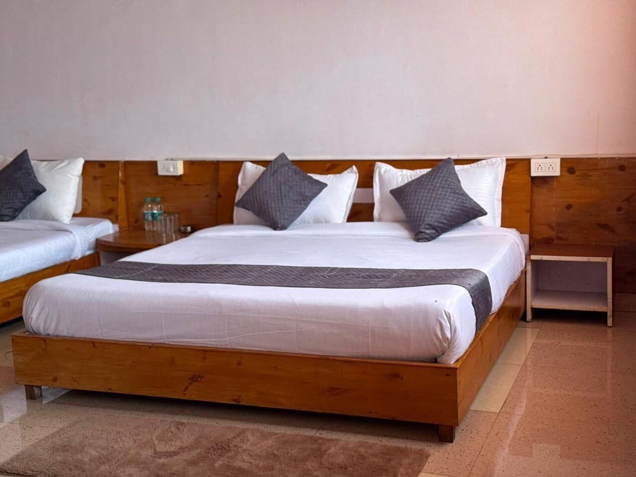 Uma cama de casal com estrutura de madeira, duas almofadas, uma mesinha de cabeceira e um criado-mudo.