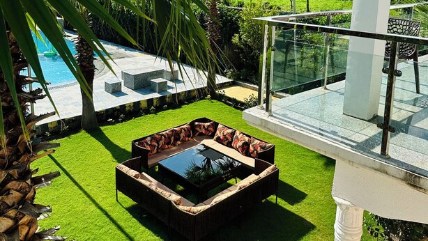 A pool area with a glass balustrade, a seating area with a glass table, and a view of a lush landscape. - The Nature View Resort (Kaladhungi)