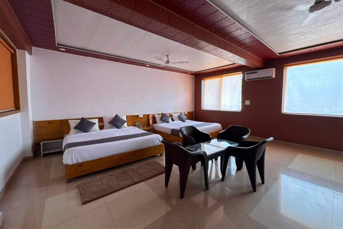 Ein Hotelzimmer mit zwei Betten, einem Tisch mit Stühlen, einem Deckenventilator und großen Fenstern.
