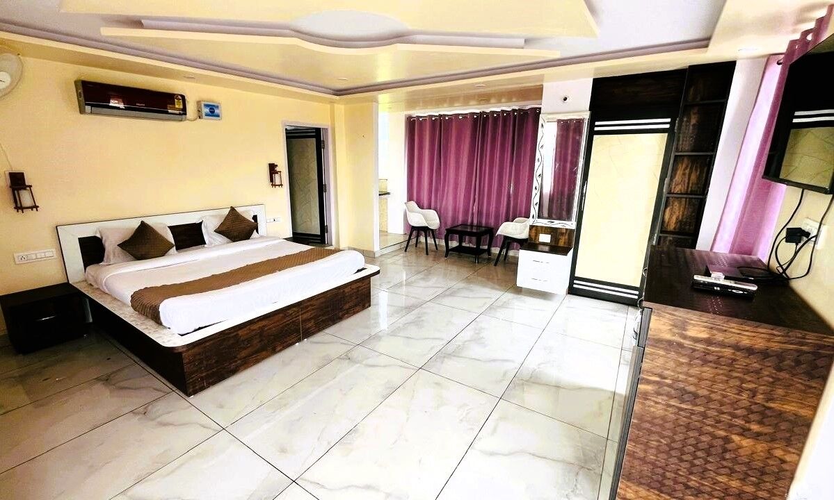 A hotel room with a large bed, a desk, a chair, a TV, and a bathroom with a shower and toilet.