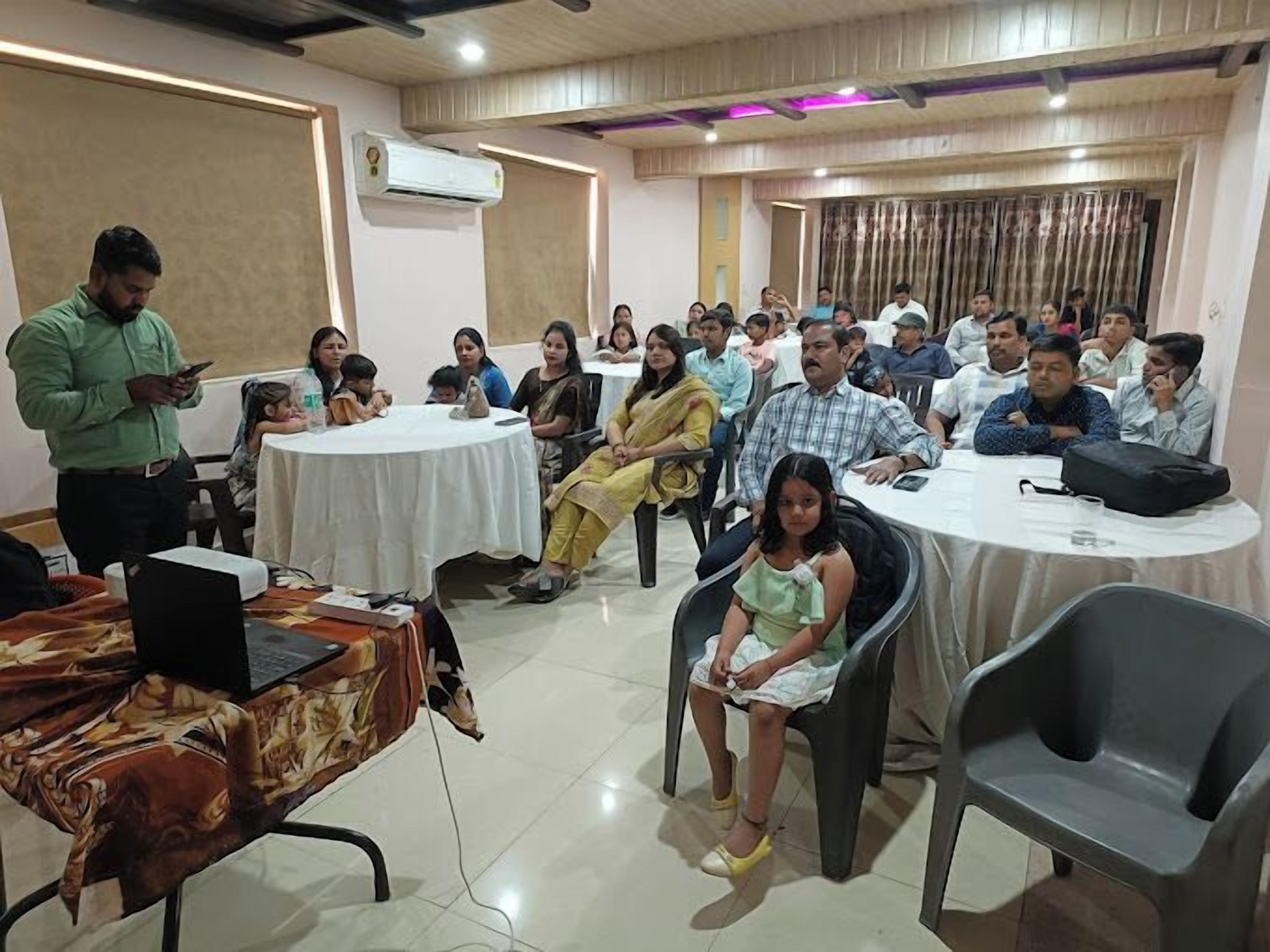 A conference room with round tables, attendees seated, and a person standing with a laptop.