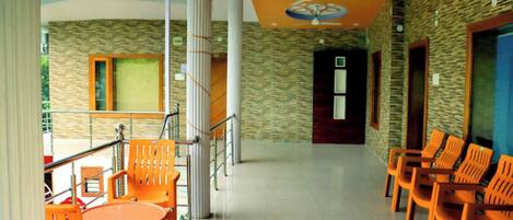 A spacious indoor area with orange chairs and tables, a staircase, and a stone wall.
