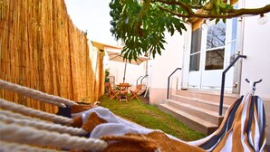 Una hamaca bajo un árbol, una valla de madera, un edificio blanco y un patio con mesa y sillas.