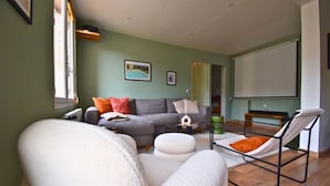 Una sala de estar con un sofá gris, sillones blancos y una hamaca.